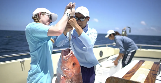 Two people holding up a fish on a boat.