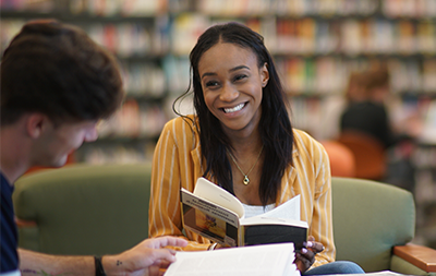 Female student holding a book smiling at a desk in the library