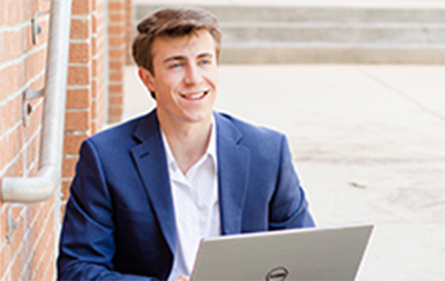 Male student working on his laptop outside